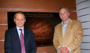 Two men standing next to each other in front of a baseball sign.