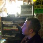 Andrew Lilley checking over the latest edit A man sitting in front of a bookshelf.