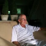 A man sitting on top of a couch in front of potted plants.