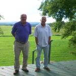 Two men standing on a deck in front of a field.