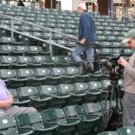 A man is sitting in the stands while filming.