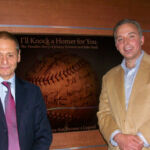 NJTV General Manager John Servidio and Producer / Director Andrew Lilley Two men standing next to each other in front of a baseball sign.